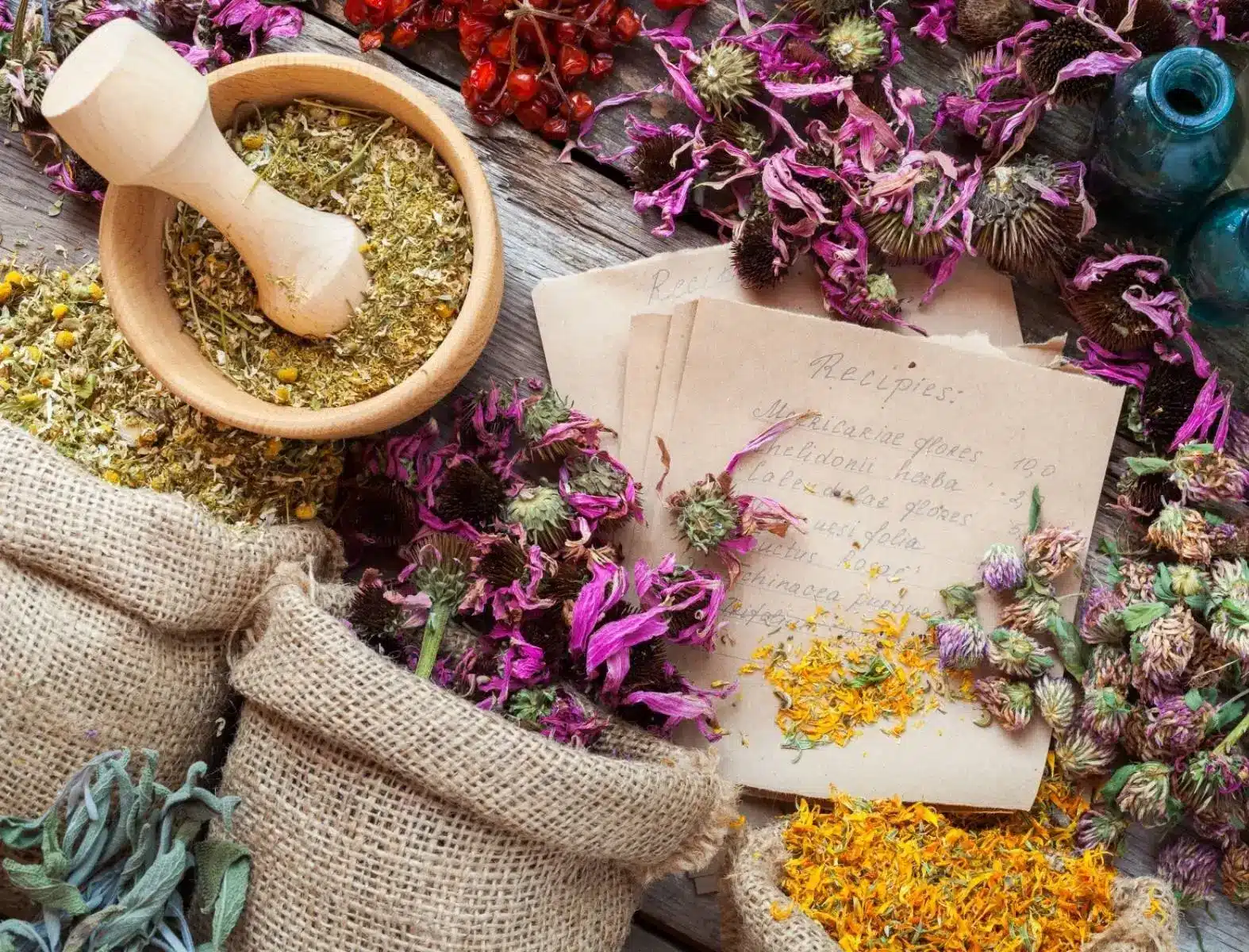 Getrocknete Heilkräuter, ein Mörsel mit Kräutern, handgeschriebene Rezepte und Glasfläschchen auf Holztisch - Homöopathie Angebot in Naturheilpraxis von Monika Tembrink in Hürth bei Köln