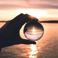 Hand hält eine Glaskugel vor einen Sonnenuntergang über einem ruhigen See, symbolisch für spirituelle Lebensberatung und Energietherapie in Hürth